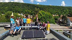 Bild zeigt Frauen* vor einer PV-Anlage auf einem Flachdach