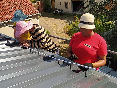 FLINTA* mit Sonnenhüten messen auf dem Dach Abstände aus